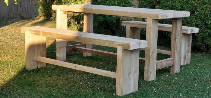 Chunky and rustic wooden garden table and benches in evening sunlight.