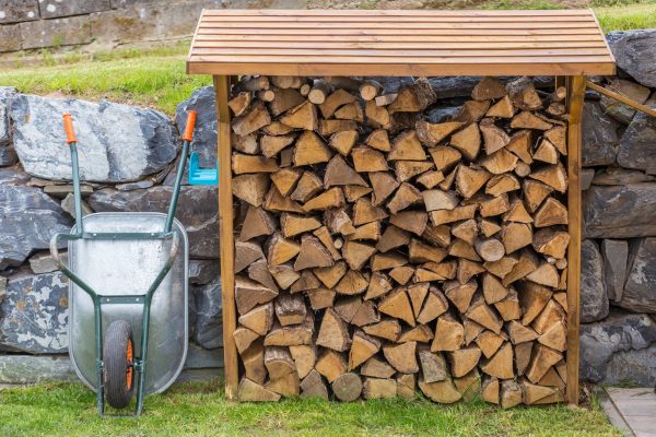 Wheelbarrow and a open shed shelter with burning fire wood with natural stones and grass on the background Wheelbarrow and a open shed shelter with burning fire wood with natural stones and grass on the background